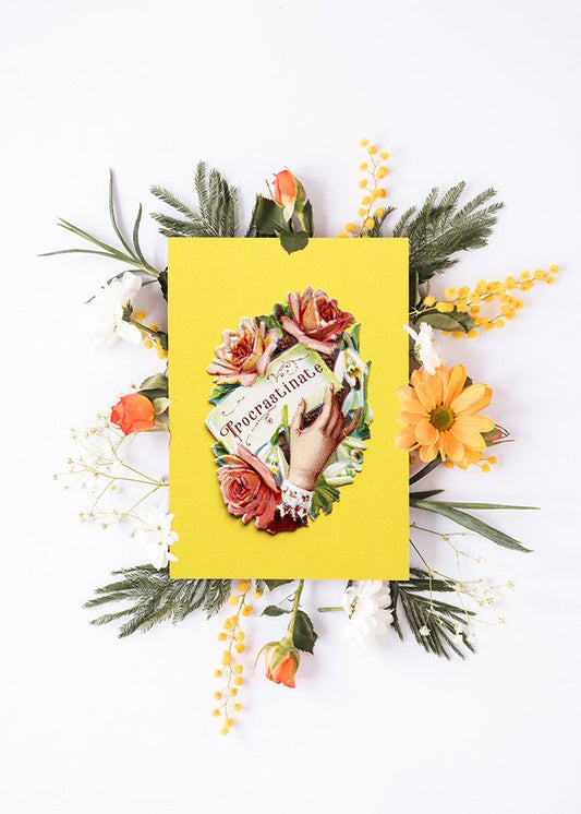 Färgglad vykort visas på ett skrivbord med en blomma bakom.